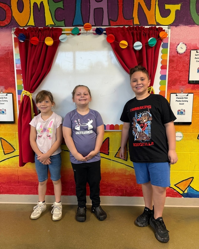 Three children stand next to each other in front of a wall with colorful backdrop and text.