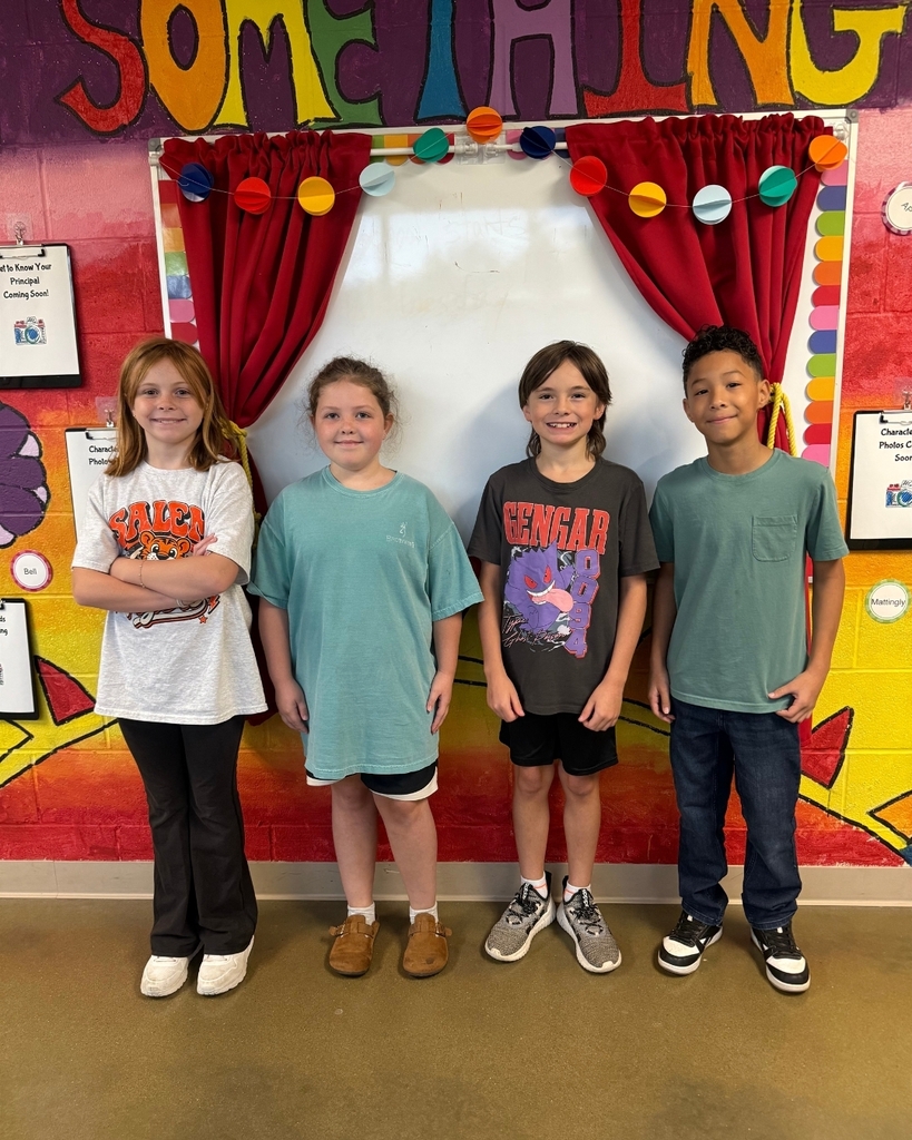 Four kids stand together in front of a colorful wall. Each wears different colored t-shirts.