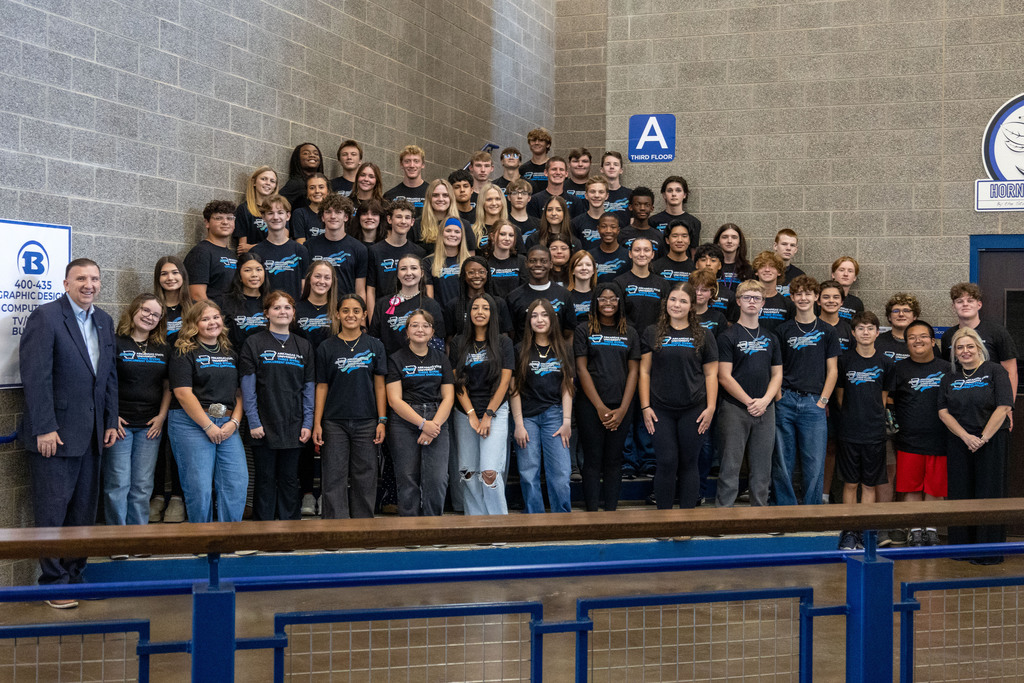 A group of people in matching black T-shirts standing in a gym with a blue railing.
