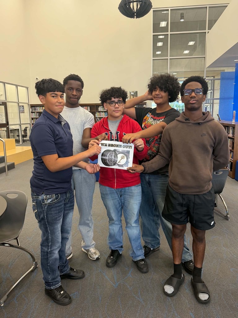 Five young men stand together in a library. One holds a poster, and they all appear to be smiling.