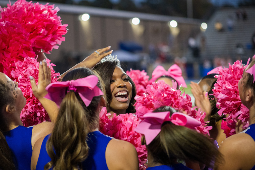 Several cheerleaders in blue uniforms with pink bows cheering at an outdoor event.