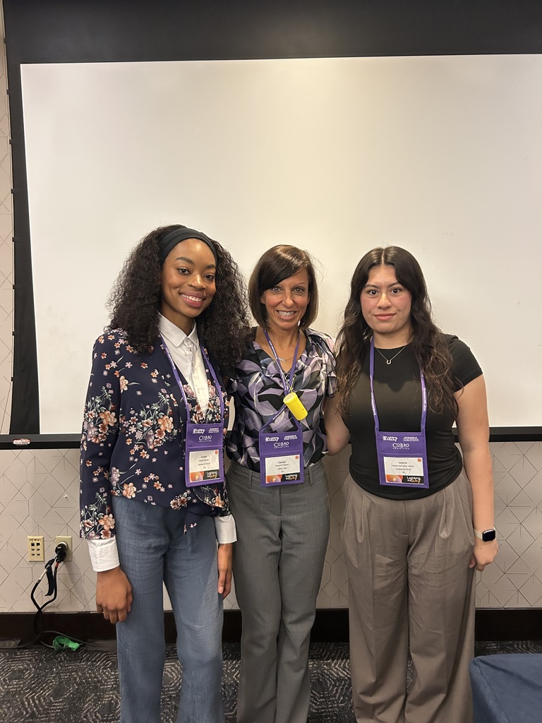 Three women with name tags pose for a picture in a room with a projector screen.