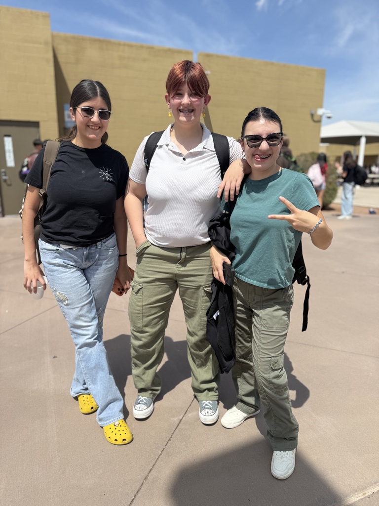 Three women in casual clothing, two with backpacks, standing outside a building with a clear sky.