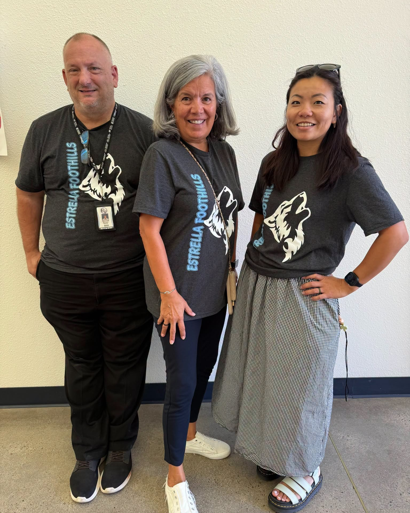 Three adults in gray T-shirts stand close together against a white wall.