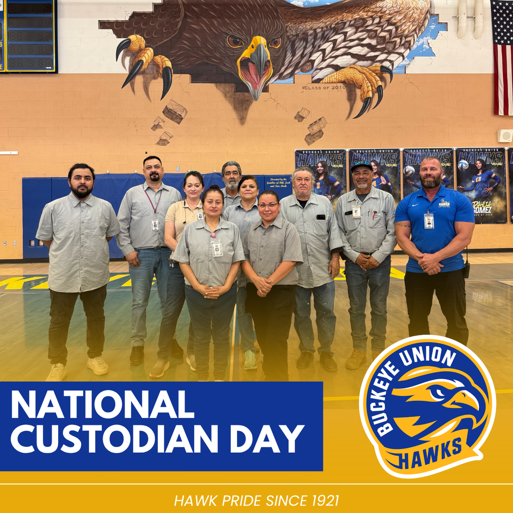Group of people in uniforms standing together in a gym. A large mural of an eagle is on the wall.