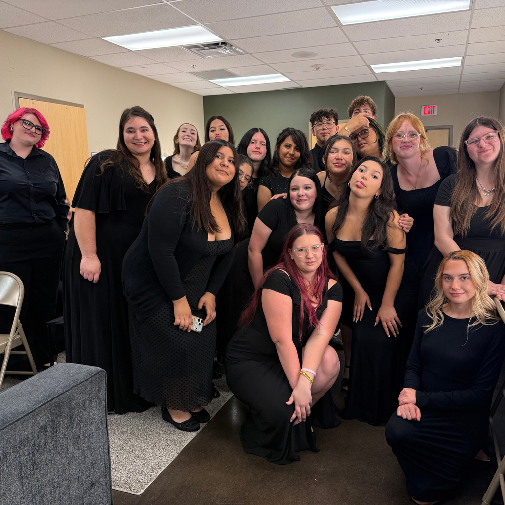 A group of women in black dresses pose for a photo in an indoor room with white walls.