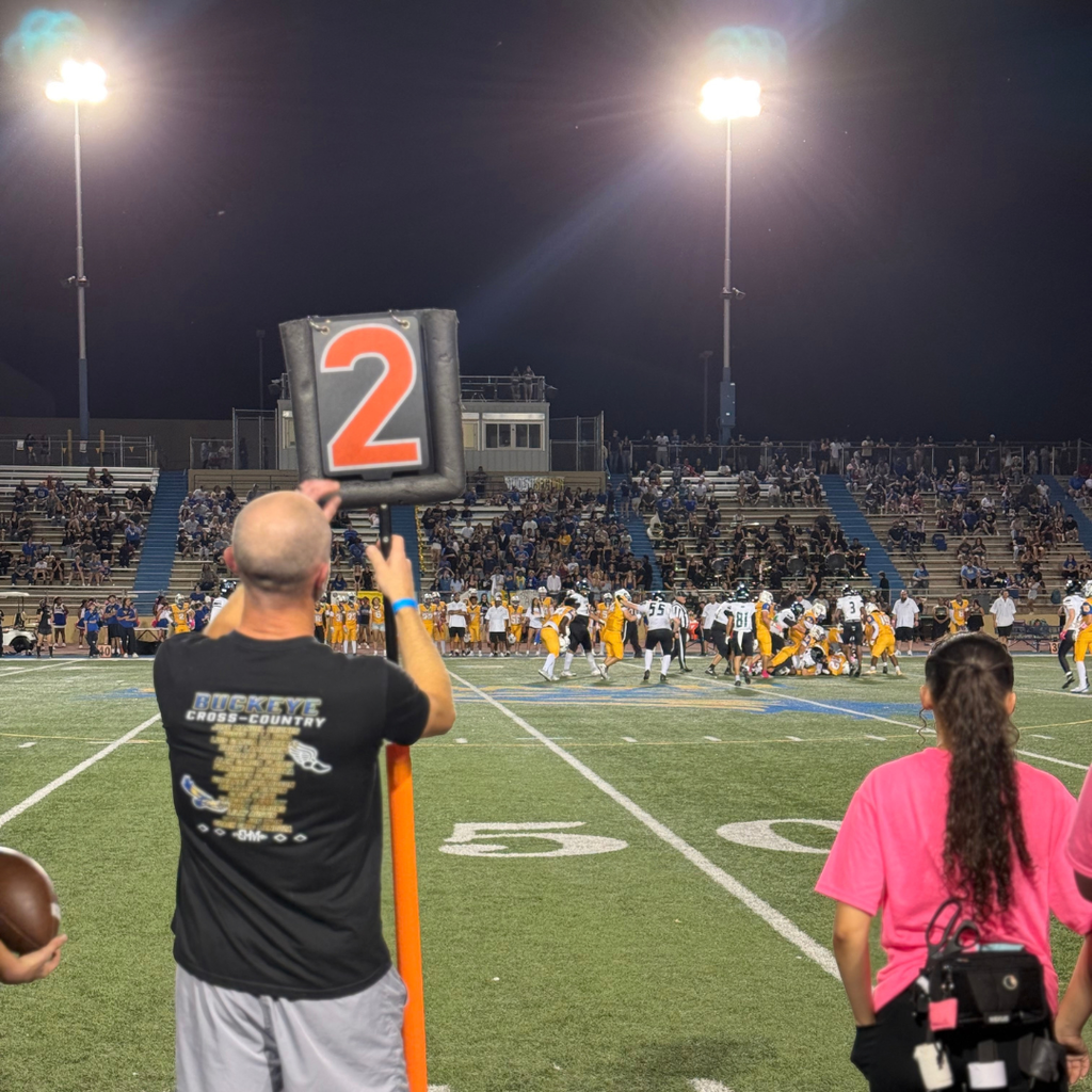 Person holding a sign on a football field. People in stands.