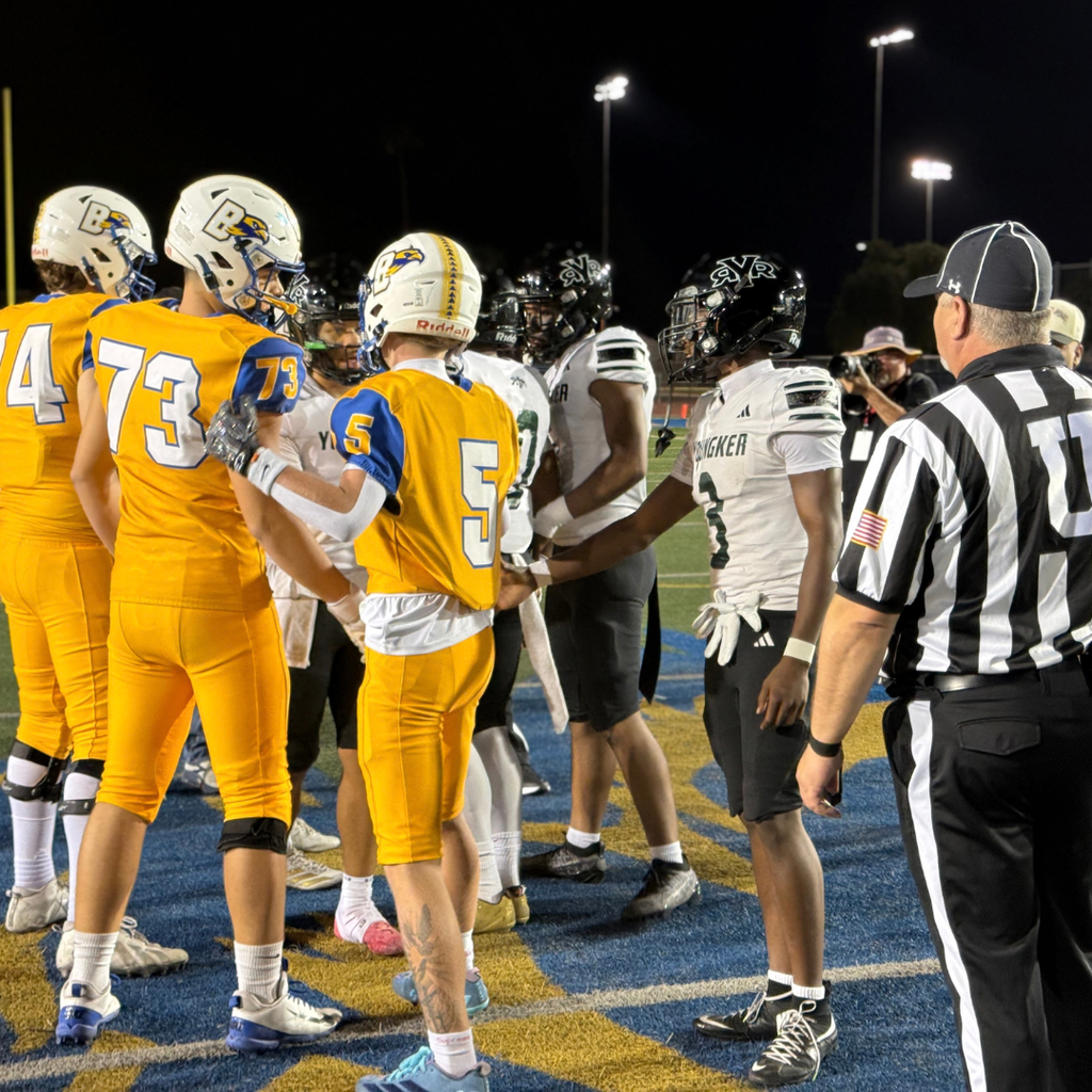 Players stand on a football field with a referee.