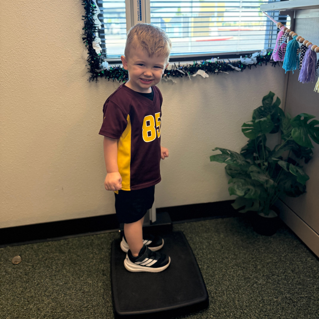 A smiling boy stands on a scale wearing a sports jersey.