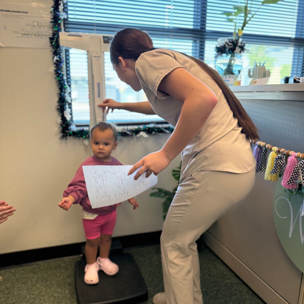A young lady with long hair checks a young girl's height while she stands on a scale.