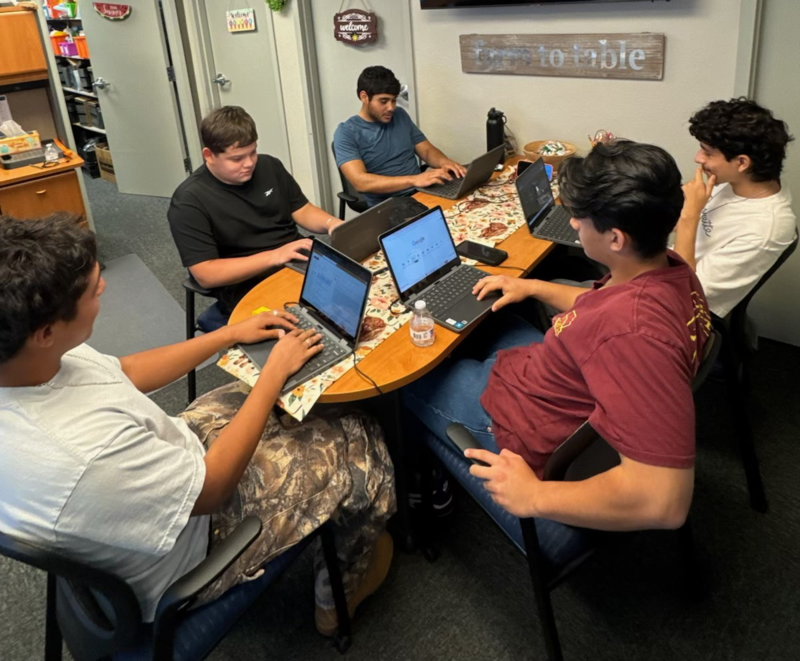 students sitting around a desk and working on computers