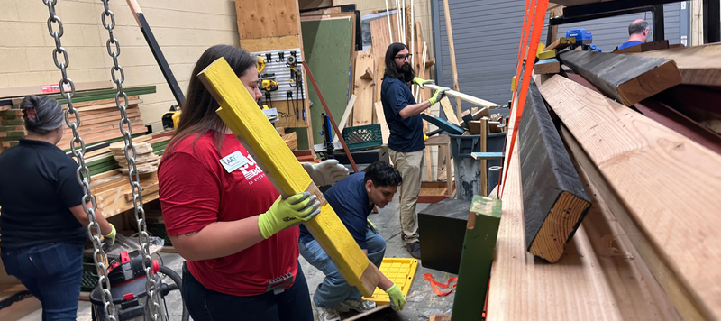 People holding lumber while cleaning in a workshop.