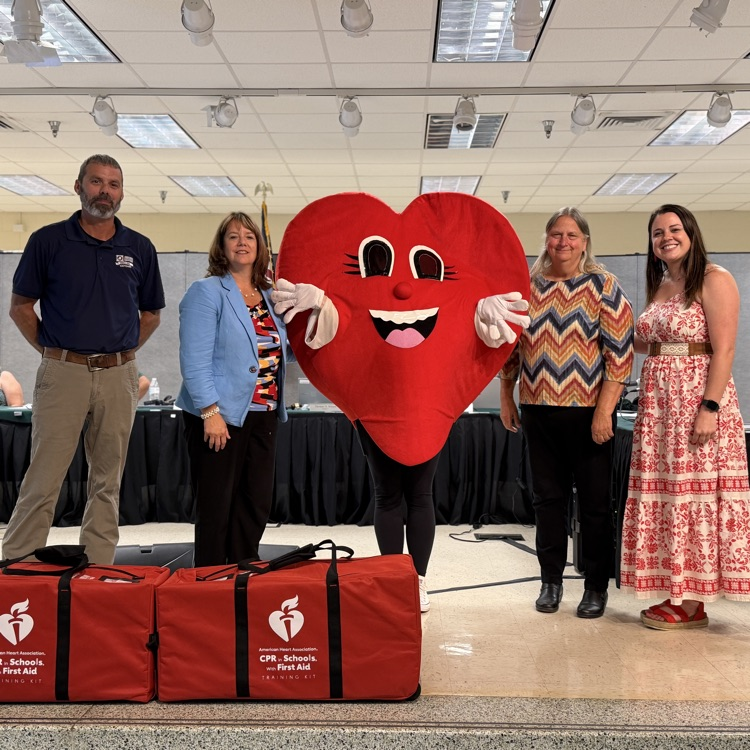 James River Equipment representative and American Heart Association presenting two CPR kits to board chair Theresa Bryant and superintendent Dr. Reasoner. American Heart Association heart mascot also pictured