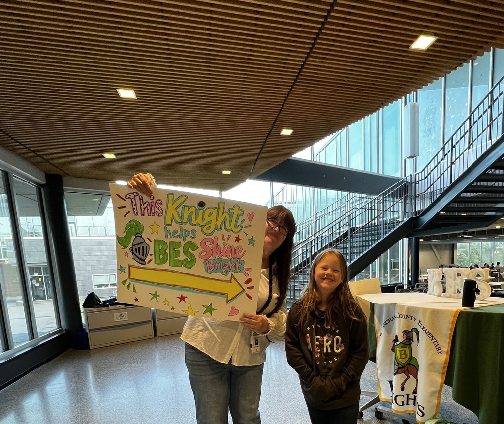 Student poses with staff and poster "This Knight Helps BES Shine Bright"