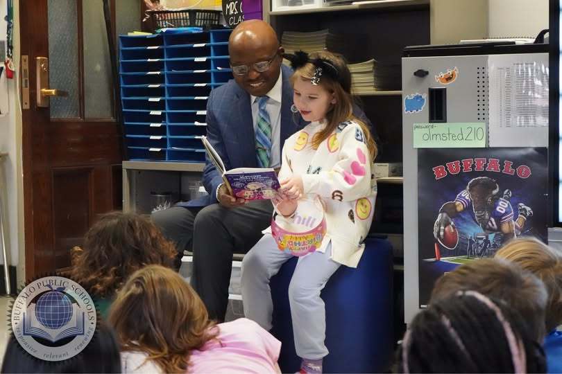 Dr. Pascal Mubenga with student reading a book in front of a class.