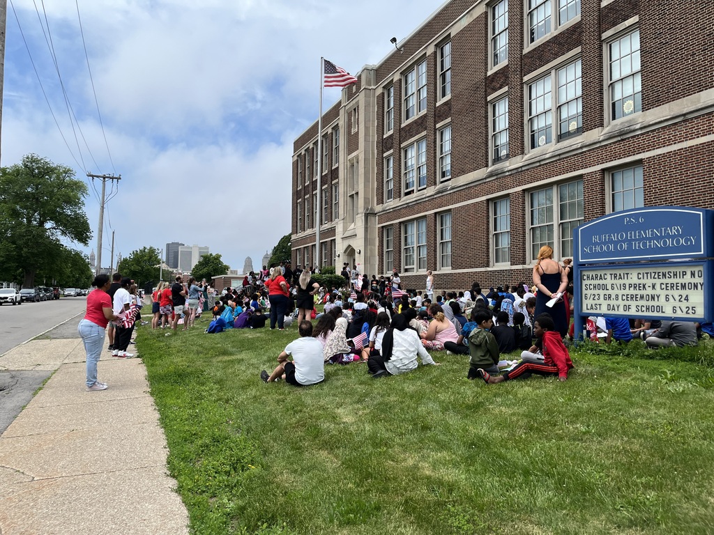 Students gathered around the flag outside of the school building