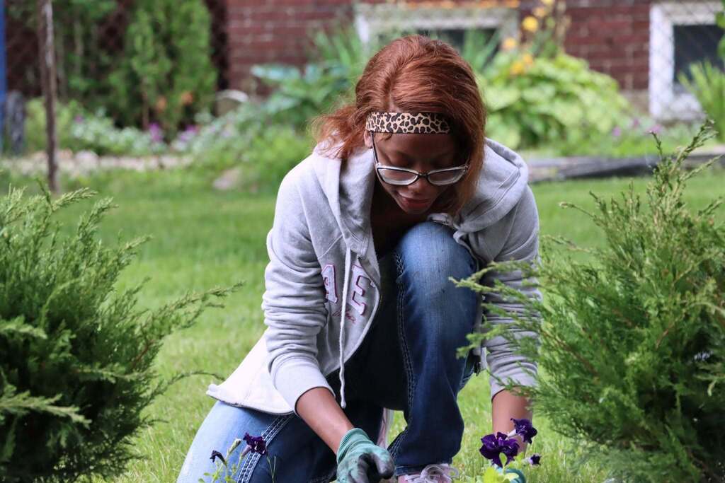 “Student plants flowers in a garden bed outdoors.”