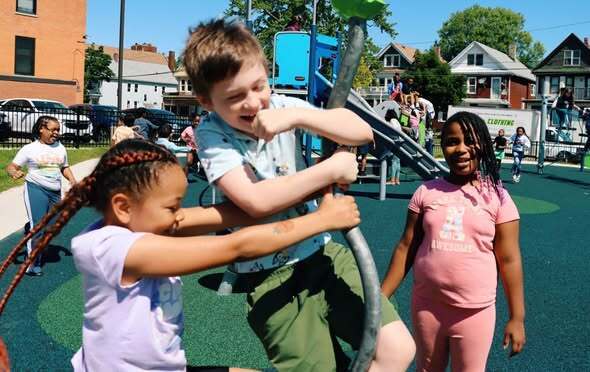Students and adults at a playground opening ribbon cutting and enjoying playground.