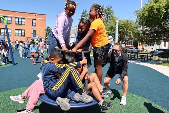 Students and adults at a playground opening ribbon cutting and enjoying playground.