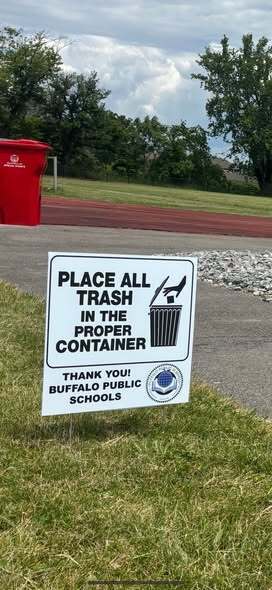 A sign that reads Place all trash in the proper container, next to a running track - Thank you Buffalo Public Schools