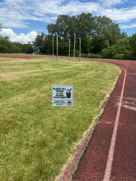 A sign that reads Place all trash in the proper container, next to a running track - Thank you Buffalo Public Schools