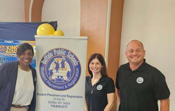 “Three individuals stand beside a Buffalo Public Schools Student Placement and Registration banner at a community resource fair. Event displays and informational booths are visible in the background.”