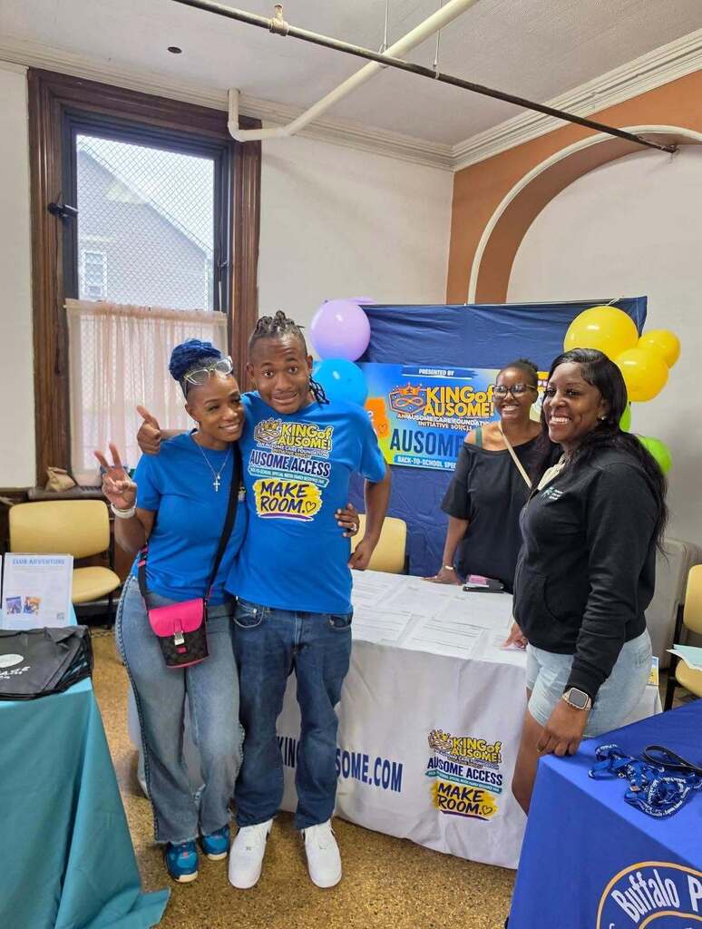 “Attendees gathered at an Ausome Access resource fair booth decorated with balloons and event signage. Information tables and community resource materials are displayed throughout the room.”
