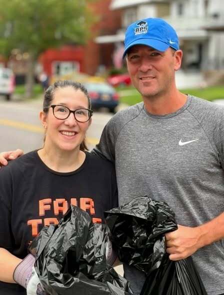 Board Members Adrianna Zullich and Erik Bohen pose outdoors holding filled trash bags during a neighborhood cleanup effort. 
