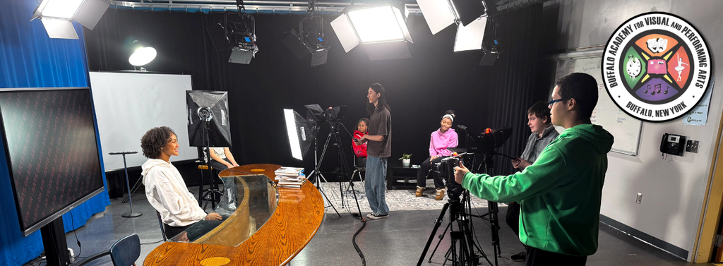 “Buffalo Academy for Visual and Performing Arts students operate cameras, lighting, and production equipment in a television studio. The image shows students participating in a hands-on media production project with a news desk, studio lights, cameras, and the school logo.”