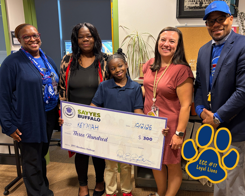 “Student poses with a ceremonial Say Yes Buffalo attendance award check for $300 alongside school staff and district representatives in an office setting. An ECC #17 Loyal Lions paw-print logo appears in the lower-right corner.”