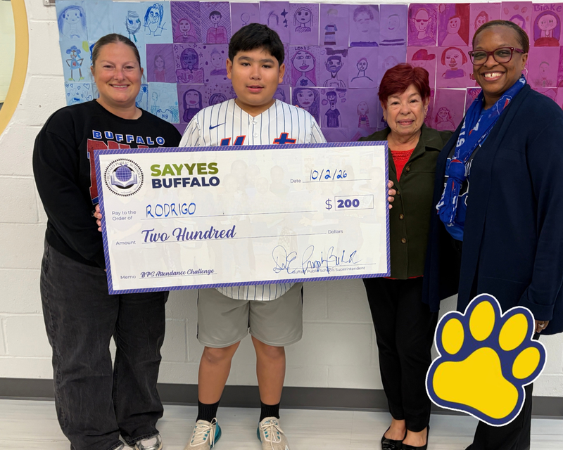 “Student holds a ceremonial Say Yes Buffalo attendance award check for $200 while posing with school staff in front of a display of student artwork. A yellow-and-blue paw-print school logo appears in the lower-right corner.”