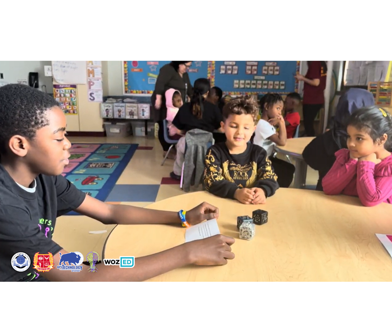 An STL sitting at a table with two young students showing them robotics