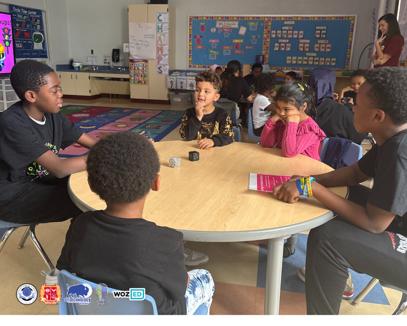 Two STLs sitting at a table with two young students showing them robotics