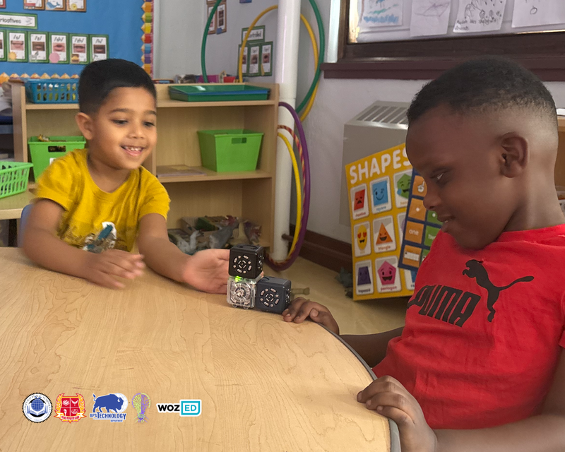 Two kindergarteners sitting at a table playing with robotics