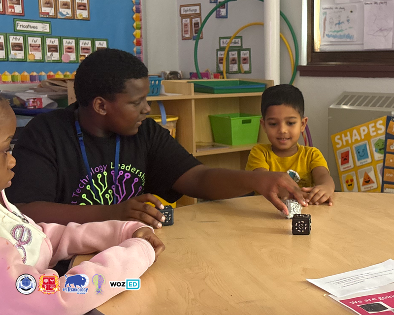 An STL sitting at a table with a young student showing them robotics