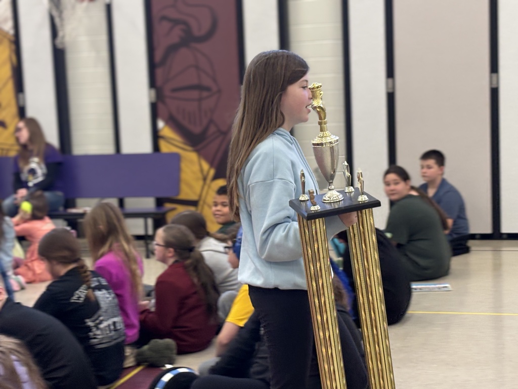 A female student walking while holding a large trophy for their classes' attendance.