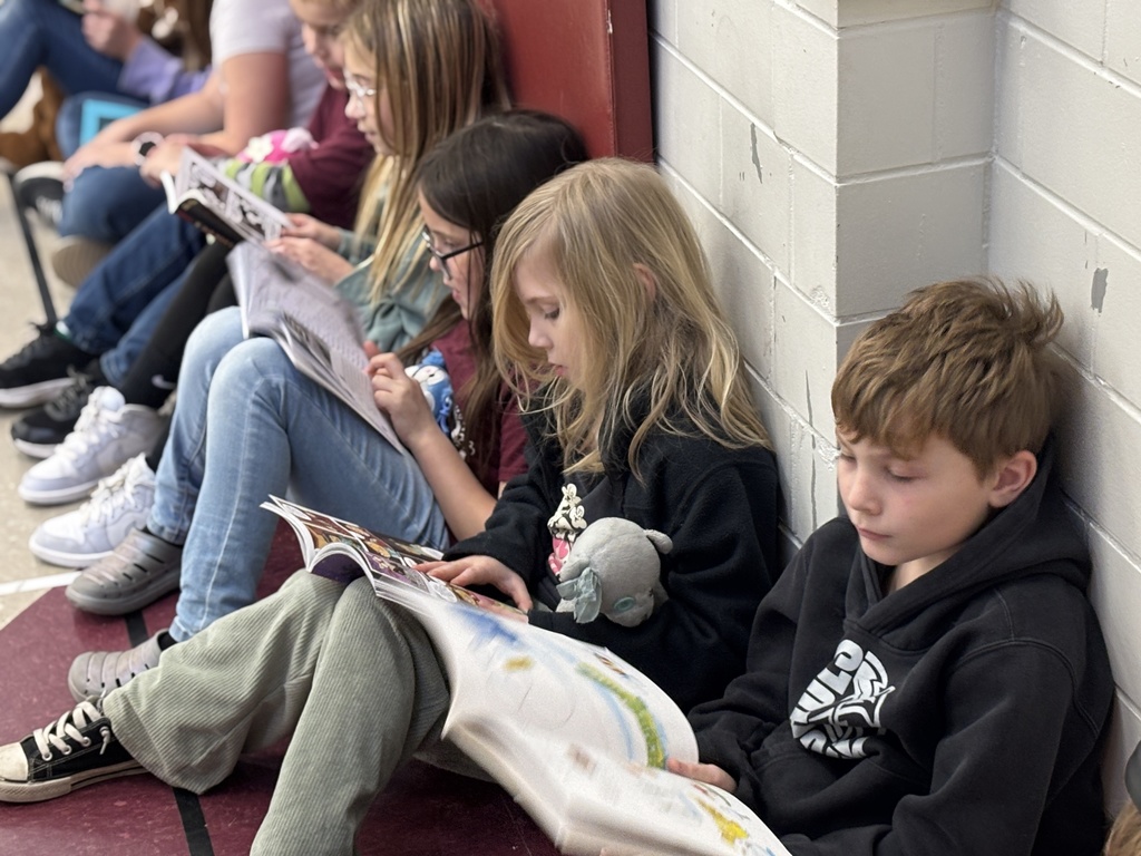 Students sitting against a wall, reading.