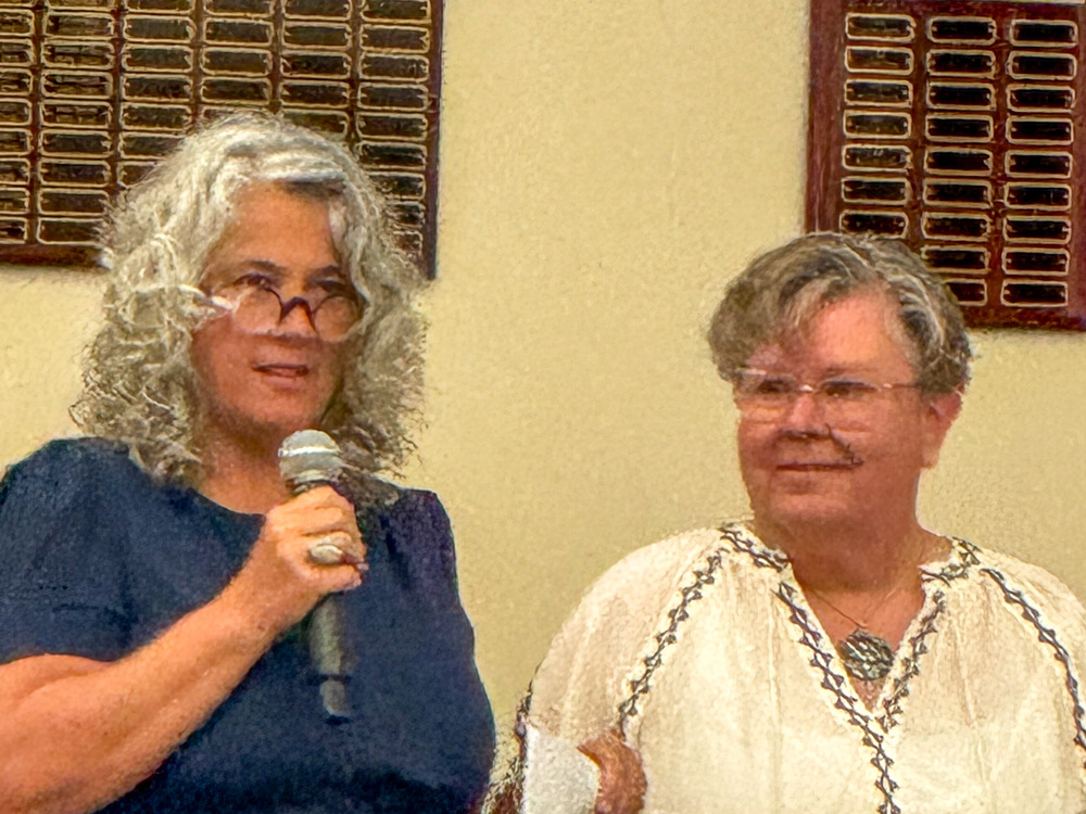 Carla Melton speaks into a microphone next to teacher Kaye Johnson.