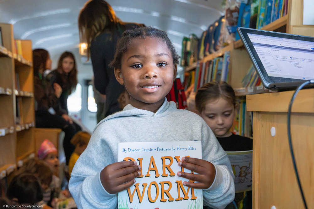 A pre-k student poses with a book in the Bookmobile.