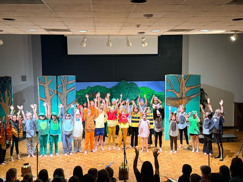 Students on stage in costumes singing and dancing. 