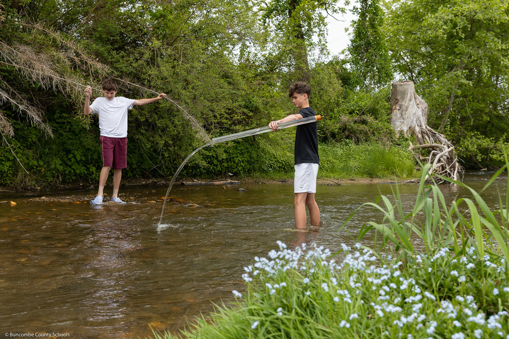 One student pours a test water sample back into the creek as another walks in the creek.