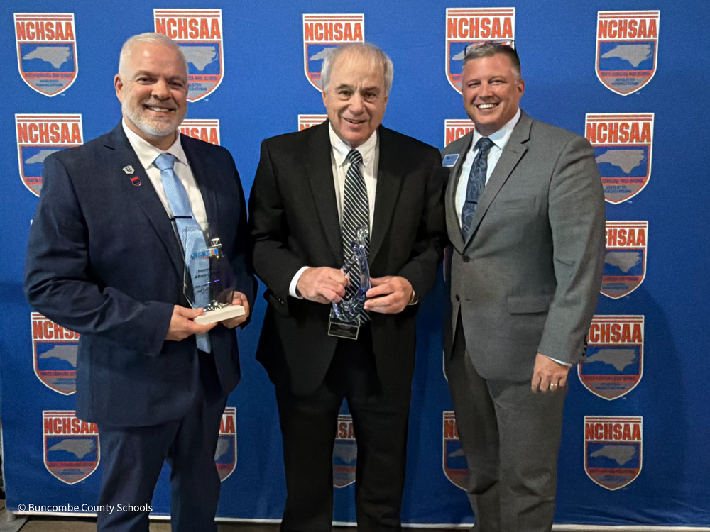 Mr. Carver and Mr. Ball stand in front of the NCHSAA banner wall, each holding their awards. BCS Assistant Superintendent Chip Cody is standing with them.