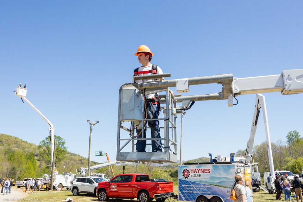A student stands in the bucket of a utility truck.
