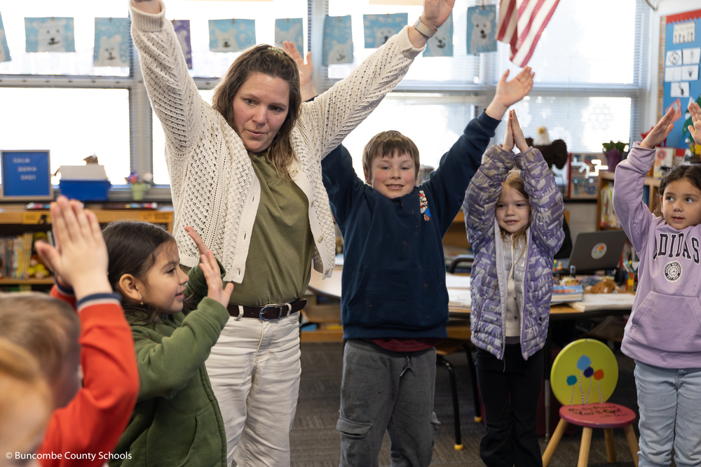 Tara Ross-Mowery doing a breathing exercise with kindergarteners. Everyone has their hands up in the air. 
