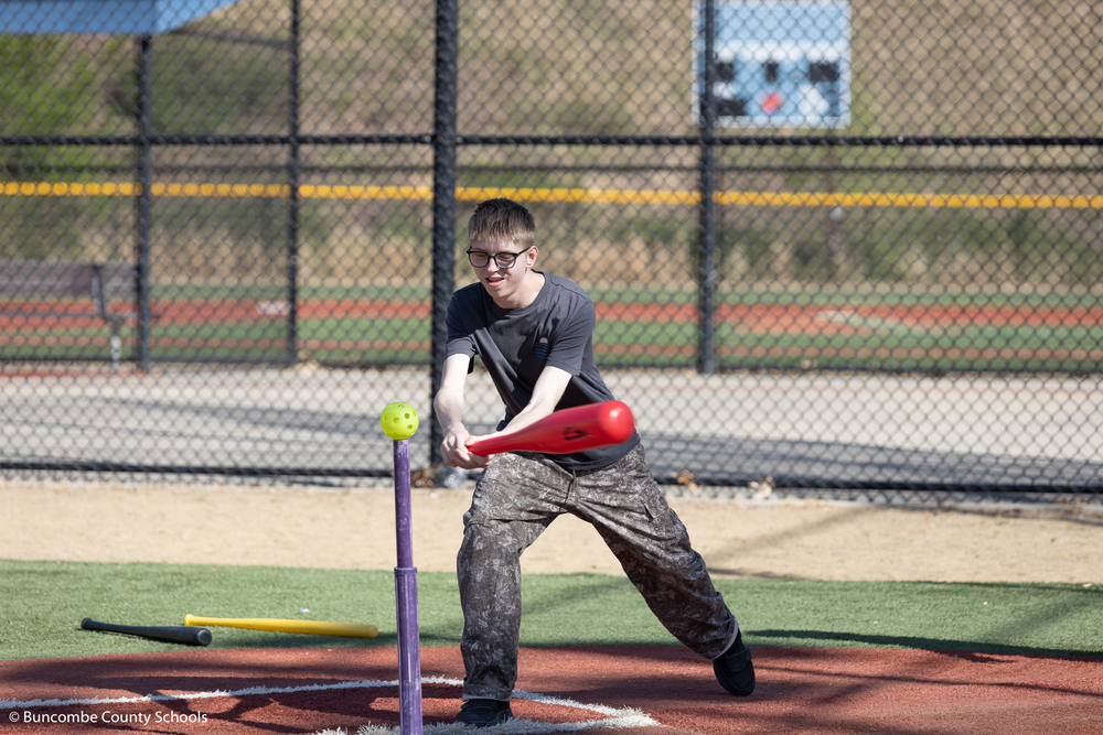 Student using a bat to hit a ball off a baseball tee. 