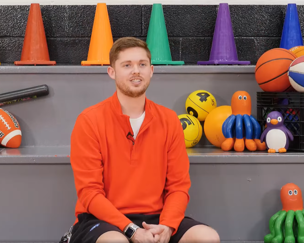 Mr. Frisby sits on bleachers surrounded by sports equipment