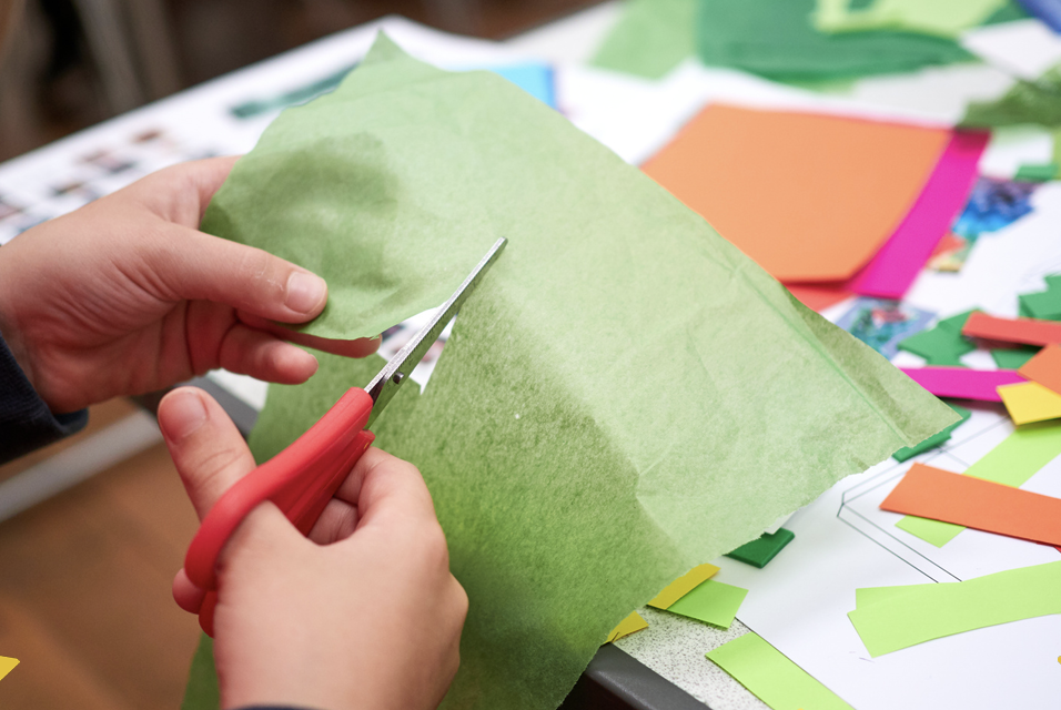 student using scissors to cut a piece of lime green tissue paper