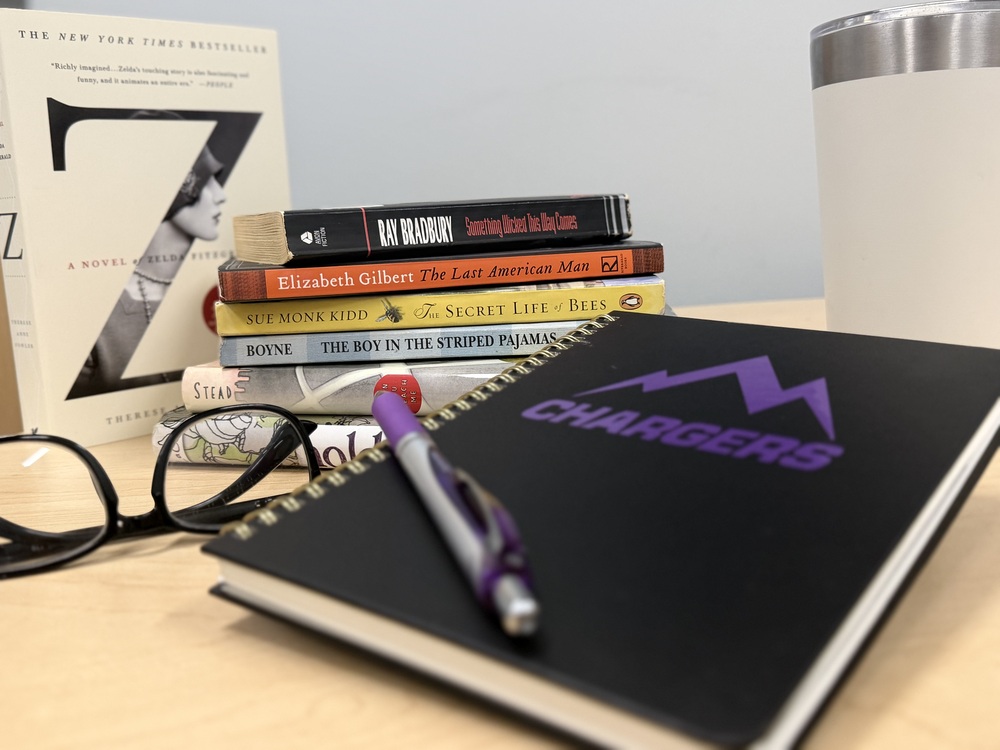 stack up books with a a cup beside them and a pair of glasses, notebook and pen in the foreground. The notebook says chargers