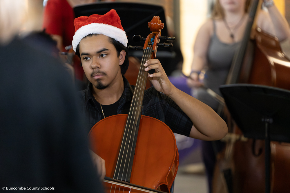 Male student looking at sheet music while he plays the cello