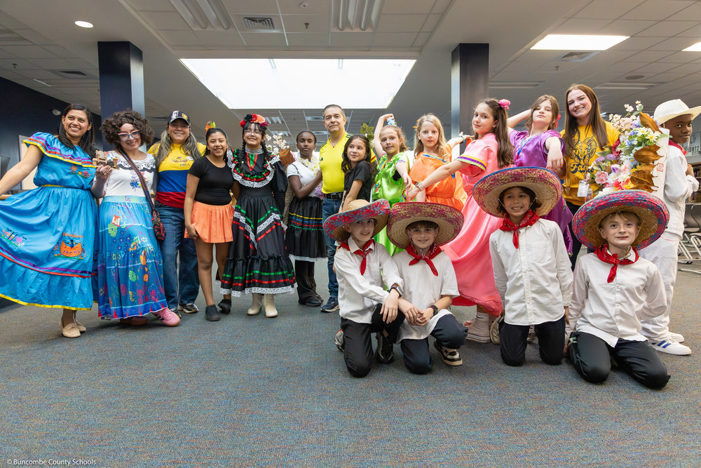 A group of adults and kids in cultural dress pose in Koontz's media center.